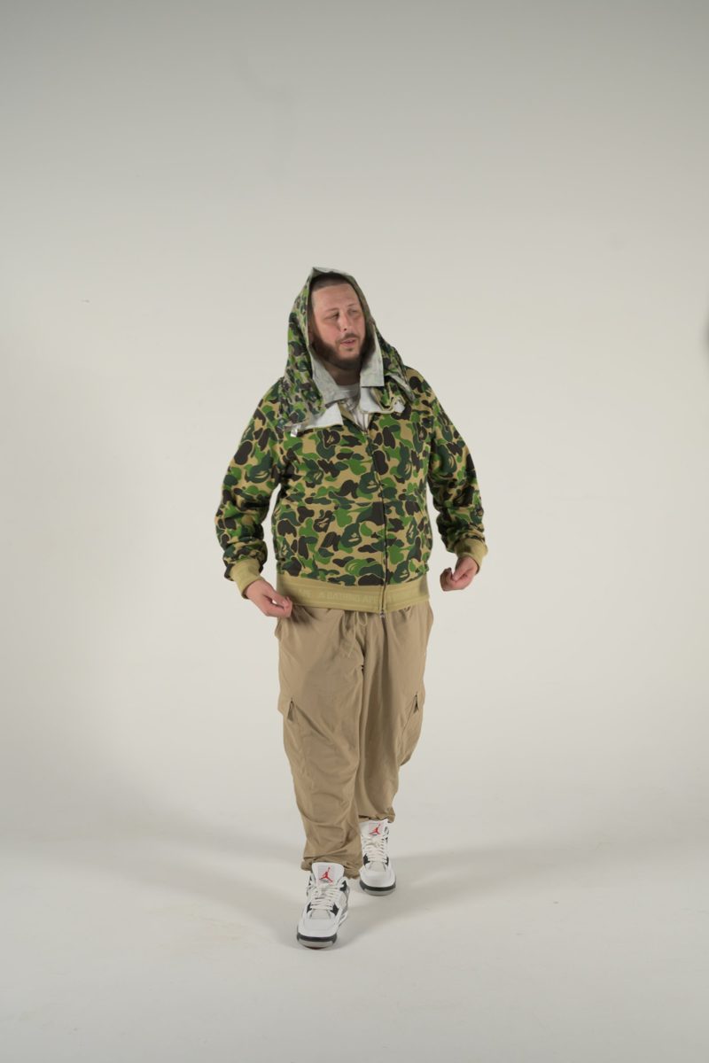Fenix walking toward the camera in a green camo zip hoodie and khaki cargos